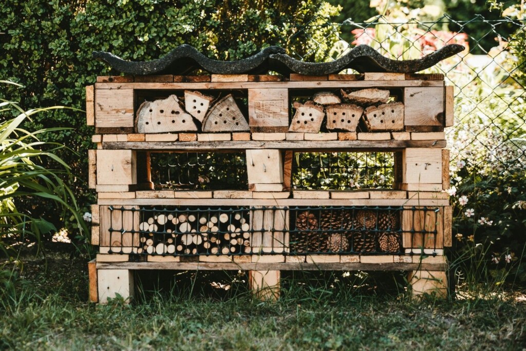 A large, handmade bug hotel made from stacked wooden pallets and filled with natural materials to attract beneficial insects