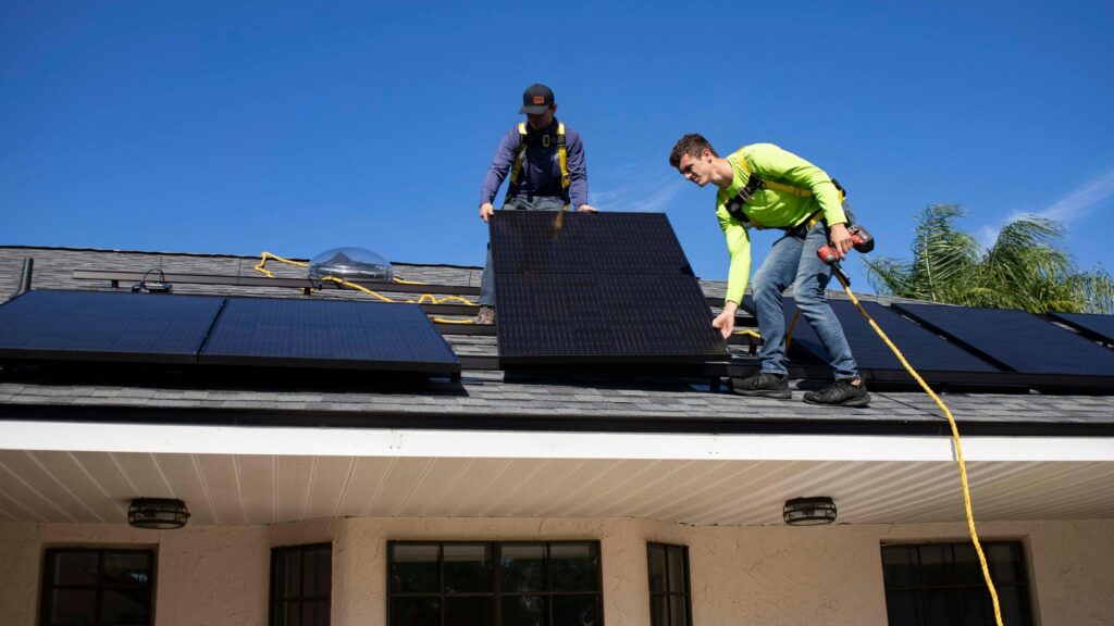 Two people installing a solar panel on a rooftop, showcasing renewable energy technology
